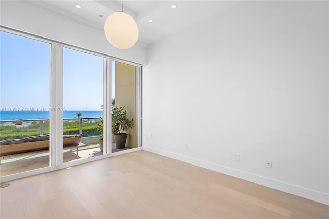 empty room with recessed lighting, a water view, baseboards, and wood finished floors