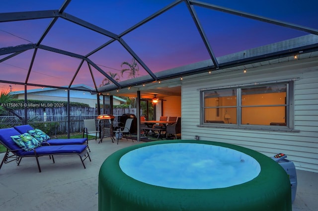 pool at dusk with a patio, fence, glass enclosure, and a ceiling fan