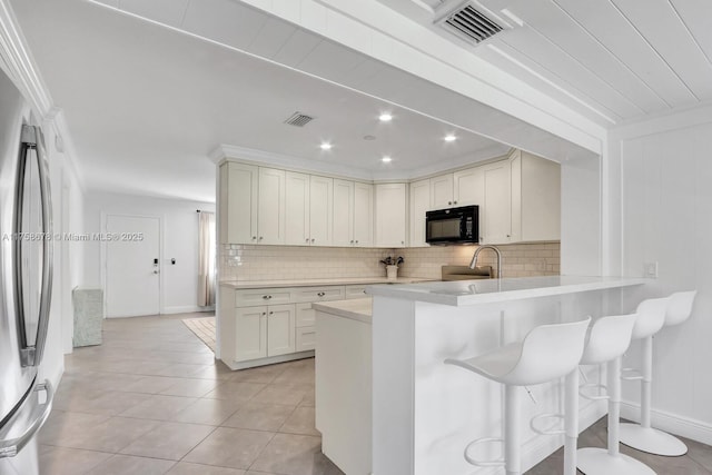 kitchen featuring black microwave, visible vents, light countertops, stainless steel refrigerator, and tasteful backsplash