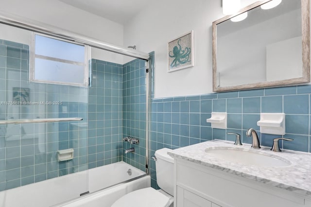 full bathroom with bath / shower combo with glass door, wainscoting, toilet, vanity, and tile walls