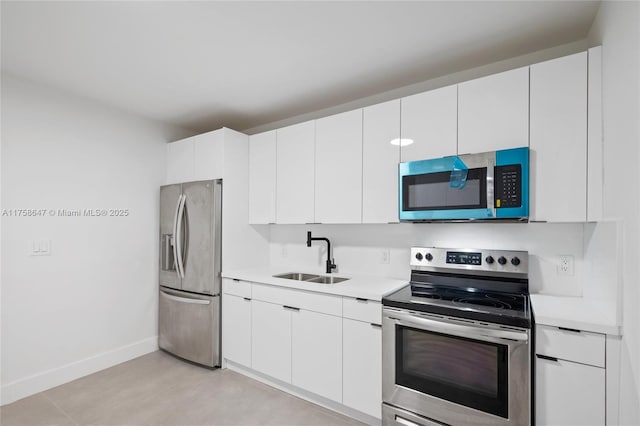 kitchen featuring appliances with stainless steel finishes, light countertops, a sink, and white cabinetry