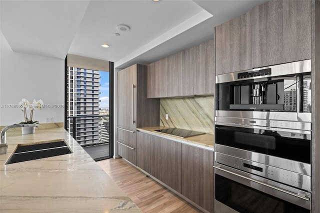 kitchen with a sink, black electric stovetop, light stone counters, and stainless steel double oven