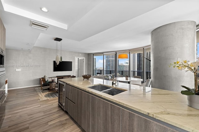 kitchen featuring wine cooler, wood finished floors, a sink, visible vents, and light stone countertops