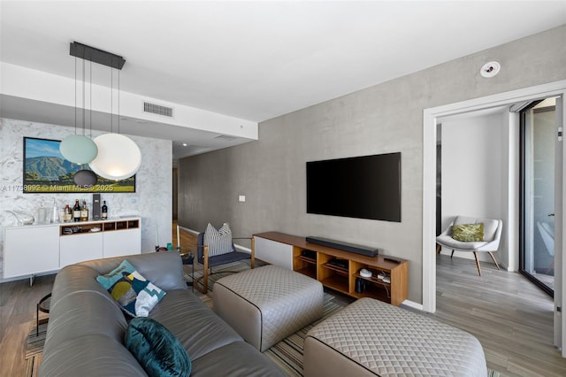 living area with a bar, light wood-style floors, an accent wall, and visible vents