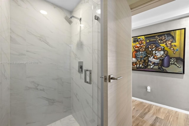 full bath with a marble finish shower, baseboards, and wood finished floors