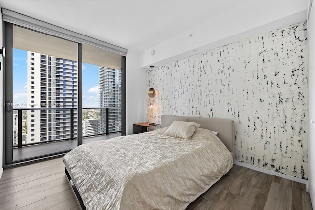 bedroom with a view of city, floor to ceiling windows, wood finished floors, access to outside, and baseboards