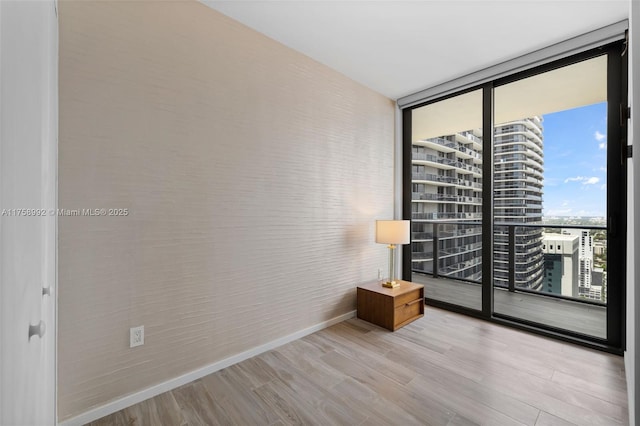 unfurnished room with a view of city, expansive windows, baseboards, and wood finished floors