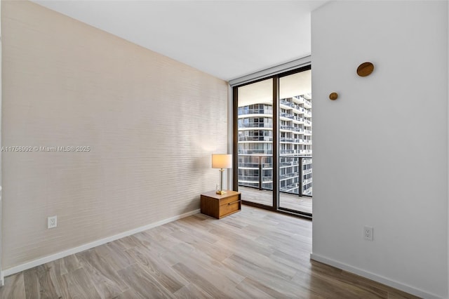 unfurnished room featuring baseboards, a wall of windows, and wood finished floors