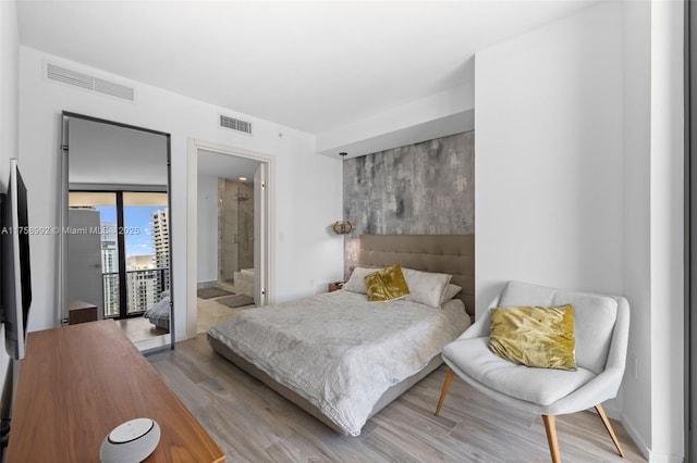 bedroom featuring ensuite bathroom, wood finished floors, visible vents, and access to exterior