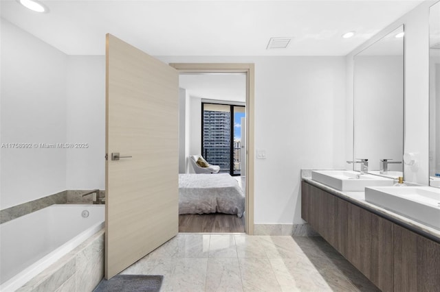 ensuite bathroom with a garden tub, double vanity, visible vents, connected bathroom, and a sink