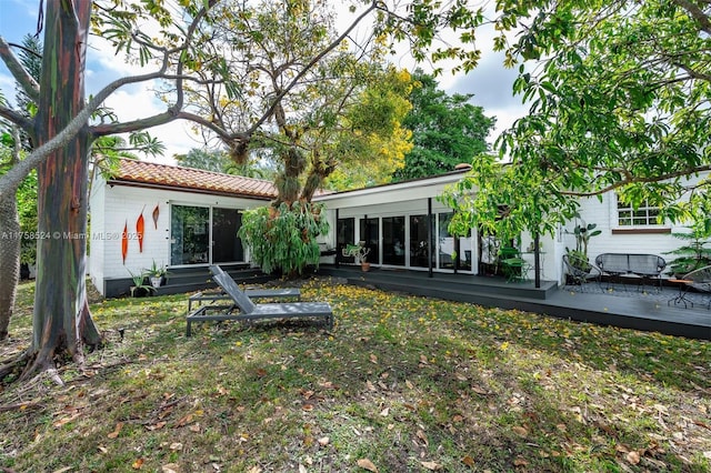 back of house featuring entry steps, a tile roof, a lawn, and a wooden deck