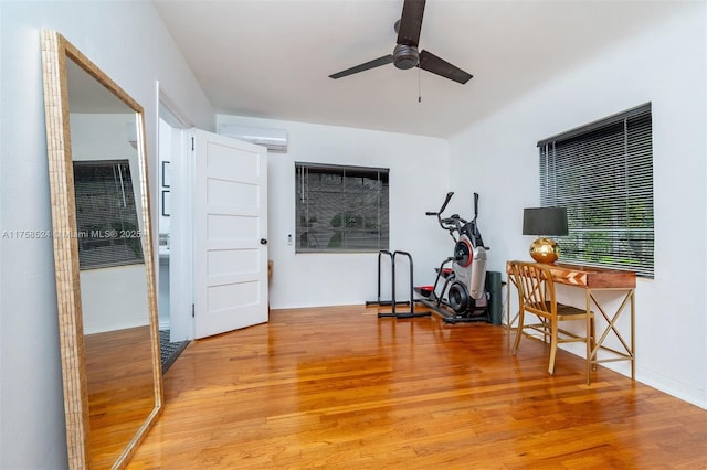 exercise room with light wood finished floors, baseboards, ceiling fan, and a wall unit AC