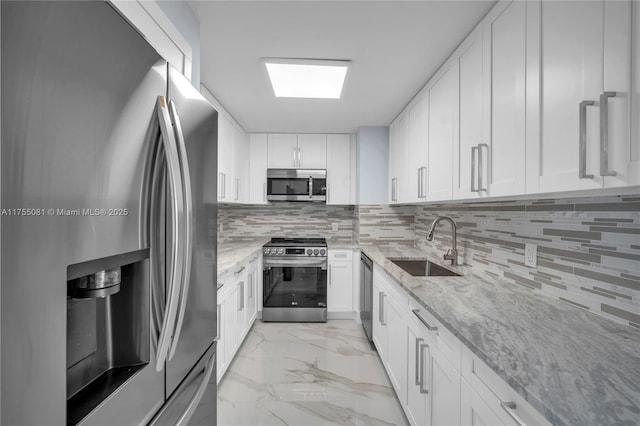 kitchen with marble finish floor, decorative backsplash, appliances with stainless steel finishes, a sink, and light stone countertops