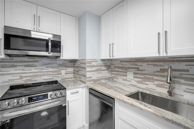 kitchen with tasteful backsplash, appliances with stainless steel finishes, white cabinetry, a sink, and light stone countertops