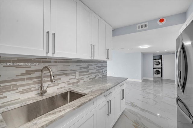 kitchen with a sink, white cabinetry, marble finish floor, stacked washing maching and dryer, and freestanding refrigerator