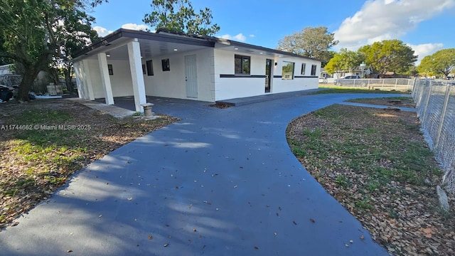 view of side of home featuring a carport, fence, concrete driveway, and stucco siding