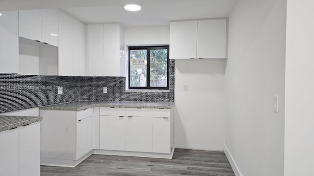 kitchen featuring baseboards, wood finished floors, light stone countertops, white cabinetry, and backsplash