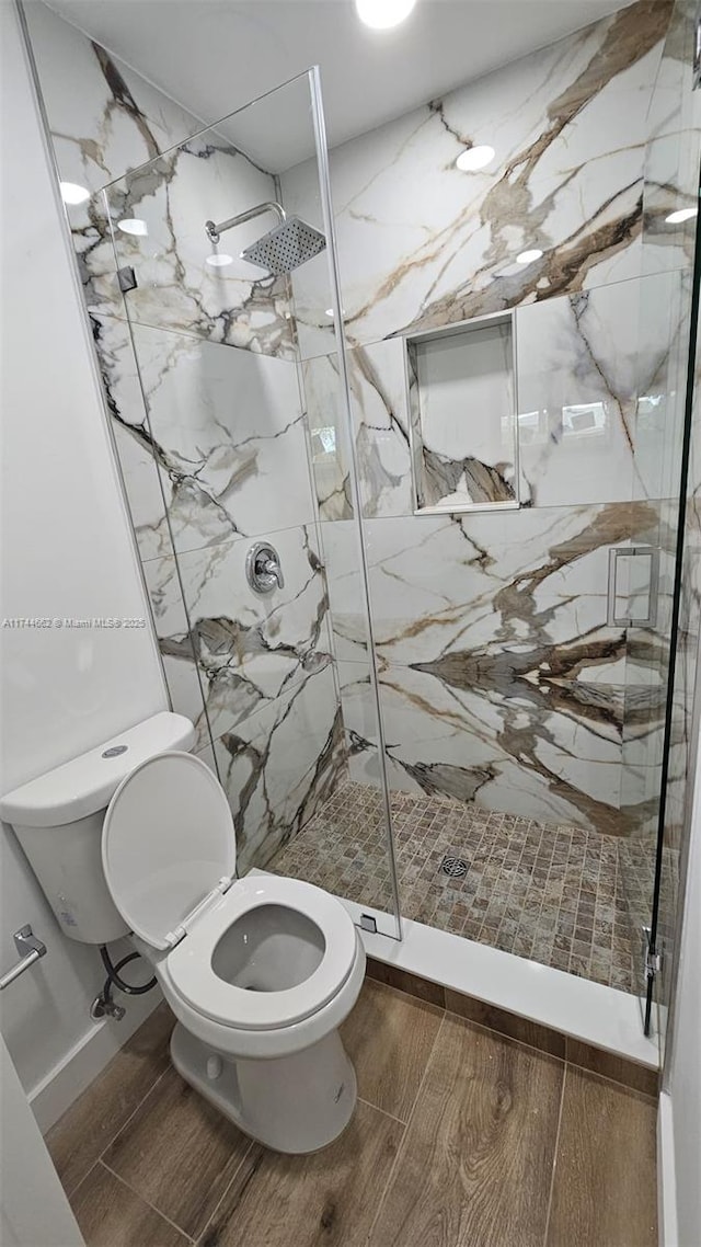 bathroom featuring wood finish floors, a marble finish shower, and toilet