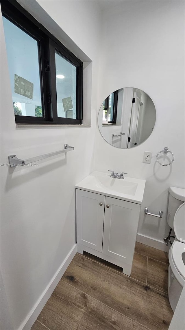 half bath with baseboards, vanity, toilet, and wood finished floors