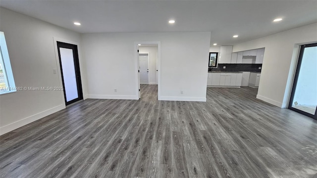 unfurnished living room featuring dark wood-style floors, plenty of natural light, and baseboards