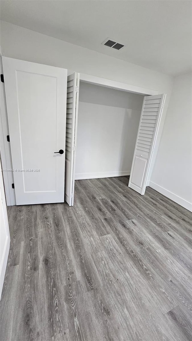 unfurnished bedroom with a closet, visible vents, baseboards, and wood finished floors