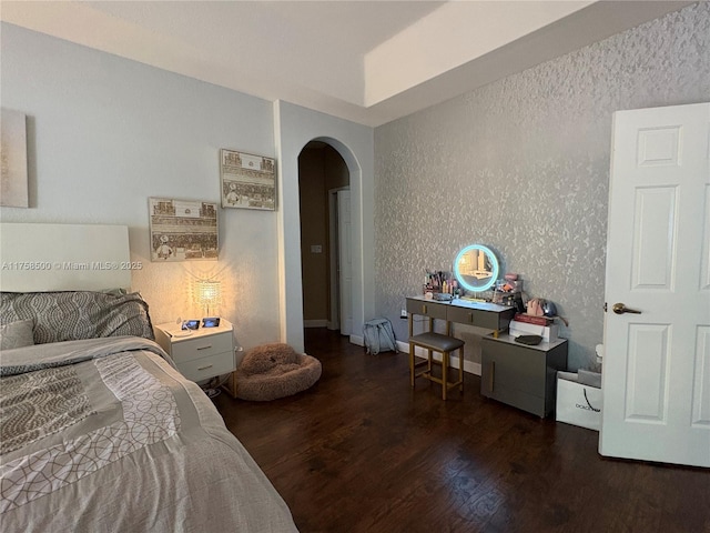 bedroom with wallpapered walls, wood finished floors, arched walkways, and baseboards