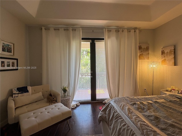 bedroom with a tray ceiling, multiple windows, and dark wood finished floors