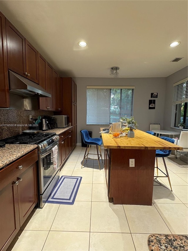 kitchen with backsplash, under cabinet range hood, a breakfast bar, light tile patterned floors, and stainless steel appliances