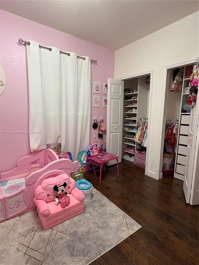 bedroom with a textured ceiling, two closets, and wood finished floors