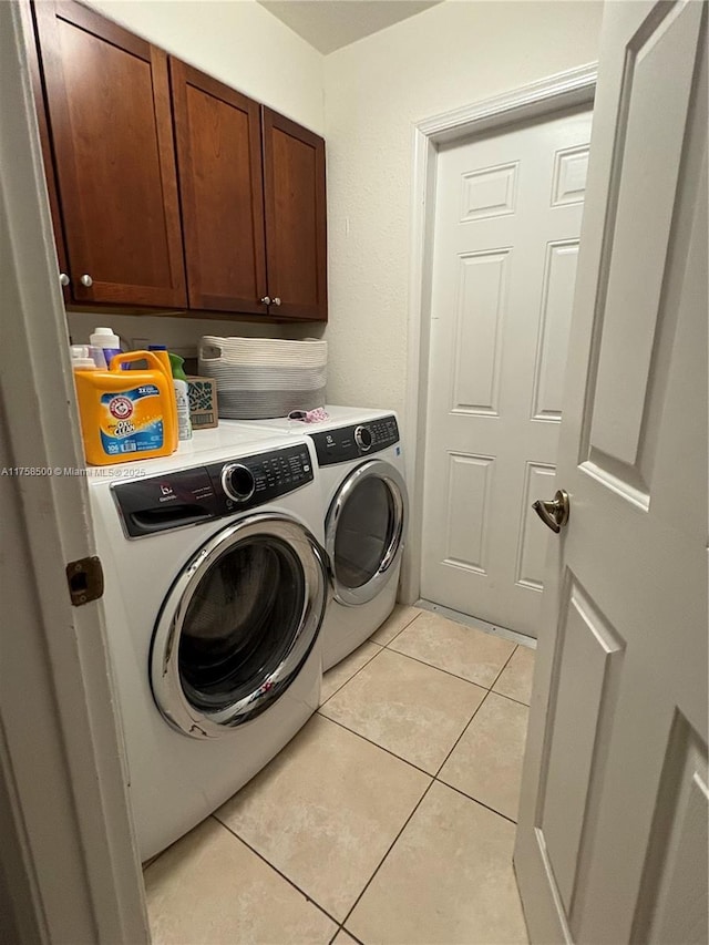 laundry room with light tile patterned floors, cabinet space, and washer and clothes dryer