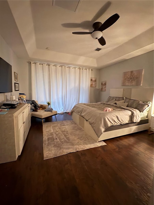 bedroom with dark wood finished floors, visible vents, a raised ceiling, and a ceiling fan