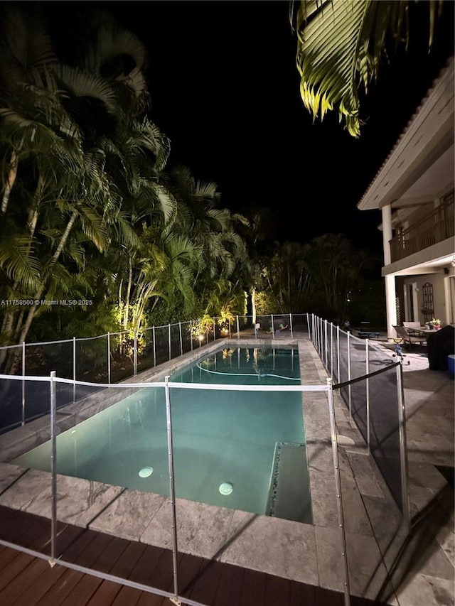 pool at night with a fenced in pool, a patio, and fence