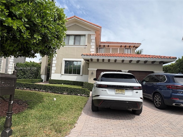 mediterranean / spanish home with an attached garage, stucco siding, a front lawn, a tile roof, and decorative driveway