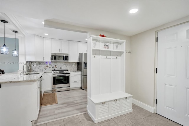 kitchen with a sink, white cabinets, hanging light fixtures, appliances with stainless steel finishes, and backsplash