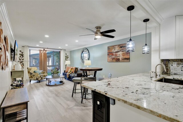 kitchen featuring beverage cooler, ornamental molding, light stone counters, decorative light fixtures, and a sink