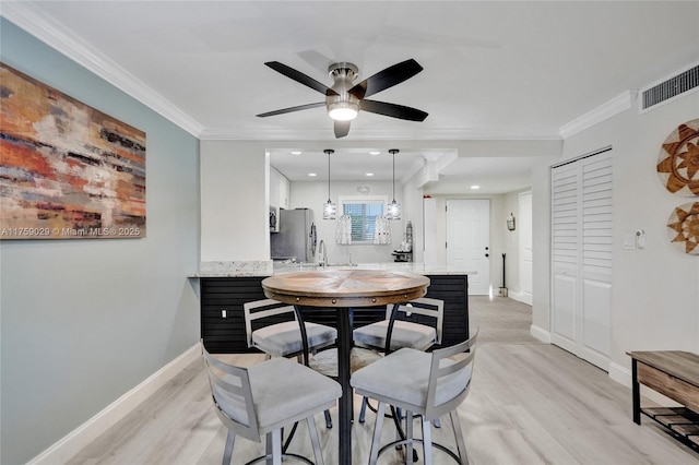 dining room with baseboards, light wood-style floors, visible vents, and crown molding