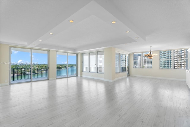 unfurnished living room with light wood finished floors, recessed lighting, a raised ceiling, an inviting chandelier, and baseboards