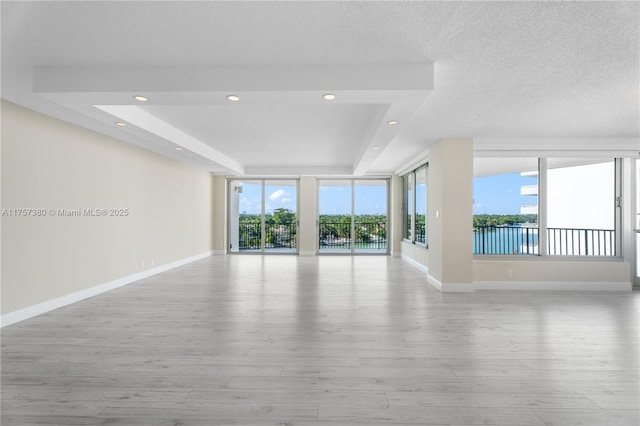 empty room featuring a tray ceiling, baseboards, wood finished floors, and recessed lighting