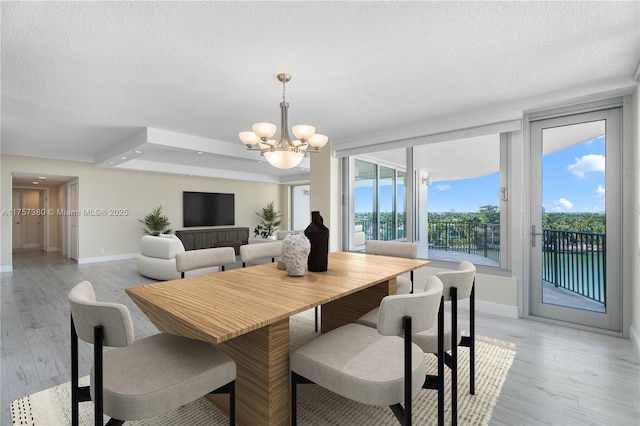 dining area with a chandelier, a textured ceiling, light wood-type flooring, and baseboards