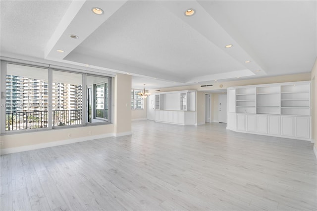 unfurnished living room with a notable chandelier, recessed lighting, a raised ceiling, light wood-style floors, and baseboards