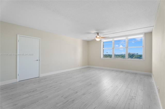 unfurnished room with a textured ceiling, light wood finished floors, and baseboards