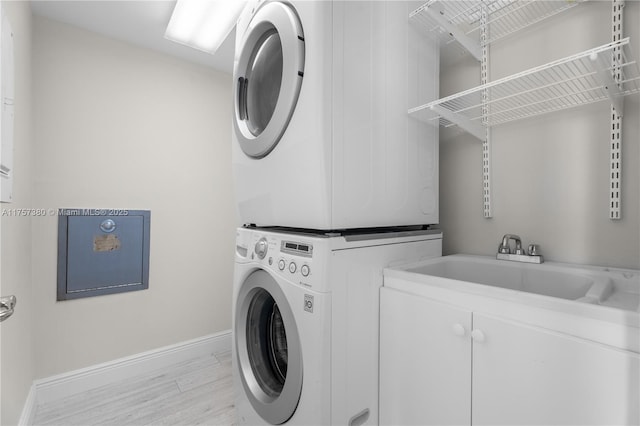 laundry area featuring light wood-style flooring, a sink, cabinet space, stacked washer / dryer, and baseboards