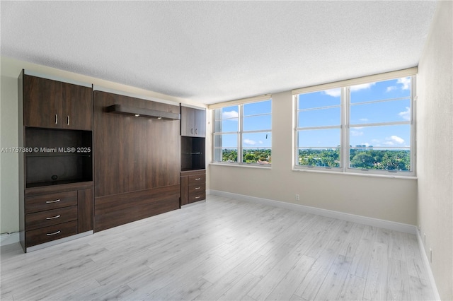 interior space with baseboards, a textured ceiling, and light wood finished floors