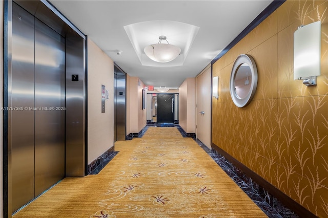 hallway with baseboards, a tray ceiling, light wood-style floors, and elevator