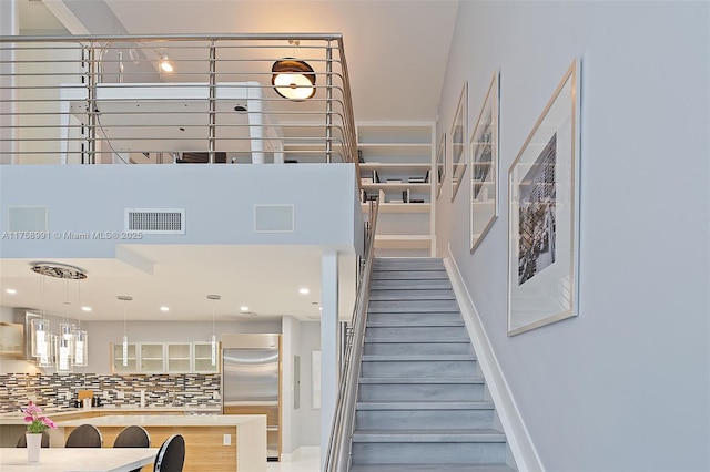 staircase with a towering ceiling, baseboards, visible vents, and recessed lighting