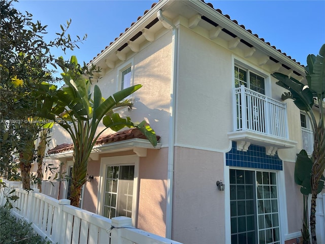 view of property exterior with a tiled roof, fence, and stucco siding