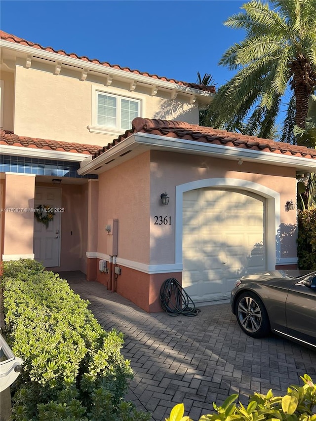 view of property exterior with a garage, a tile roof, decorative driveway, and stucco siding