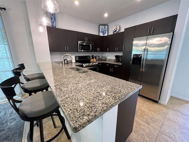 kitchen with light stone counters, stainless steel appliances, a peninsula, a sink, and a kitchen breakfast bar