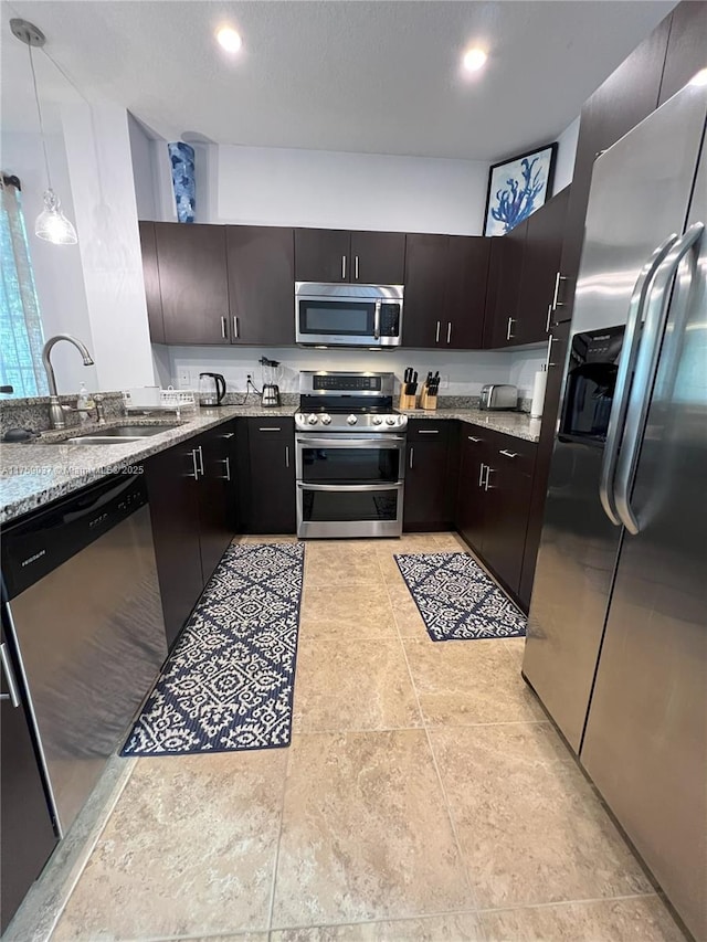 kitchen featuring light stone counters, recessed lighting, stainless steel appliances, a sink, and pendant lighting