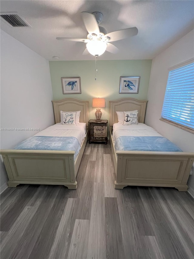 bedroom featuring a ceiling fan, baseboards, visible vents, and wood finished floors